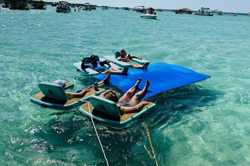 People relaxing on floating platforms in clear turquoise water, with boats in the background. 5