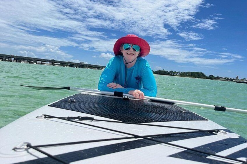 Een persoon staat op een paddleboard in het water, met een steiger op de achtergrond. 3