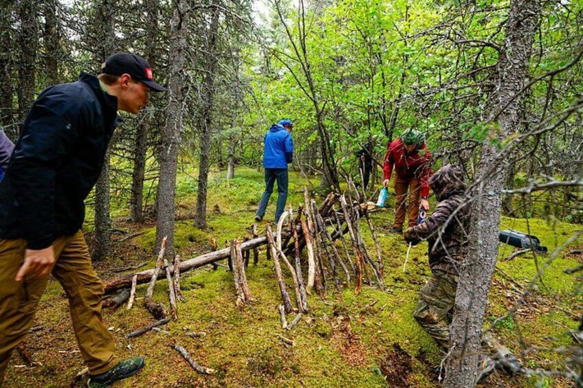 Människor på en glänta i skogen, omgiven av fallna träd, och en person klädd i kamouflagekläder. 3