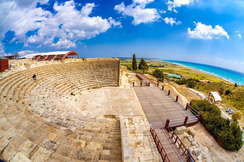 Un ancien amphithéâtre doté de gradins en pierre et d’une scène, offrant une vue panoramique sur un paysage côtier composé de champs et d’une plage. 1