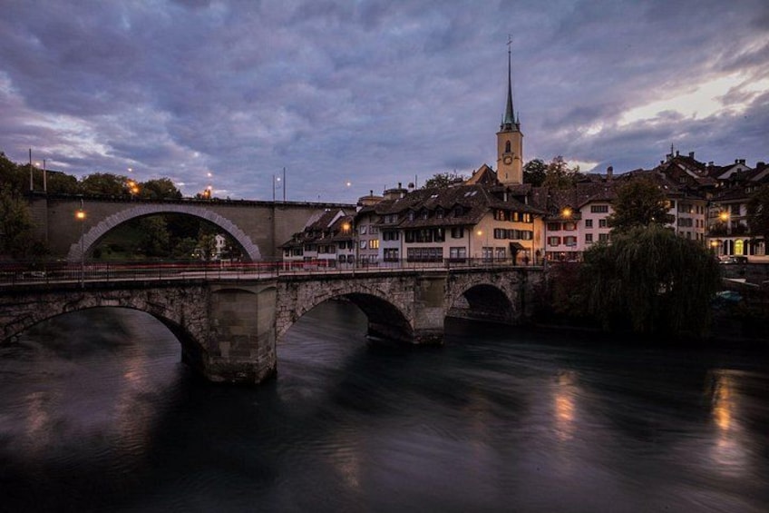 A stone bridge over a river, a church with a spire, and buildings along the riverbank. 2