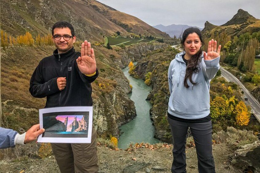 Two people standing on a rocky outcrop with a river and mountains in the background. 2