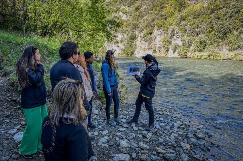 A group of people standing by a river, one person holding a tablet. 2