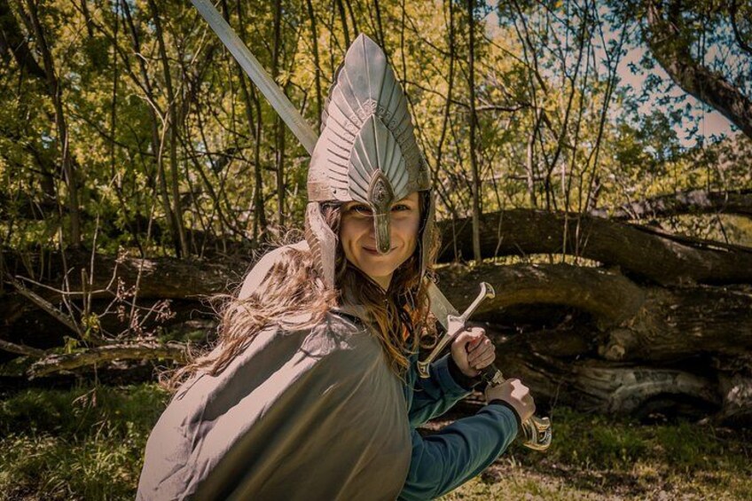 A person in a forested area wearing a helmet and holding a sword. 3