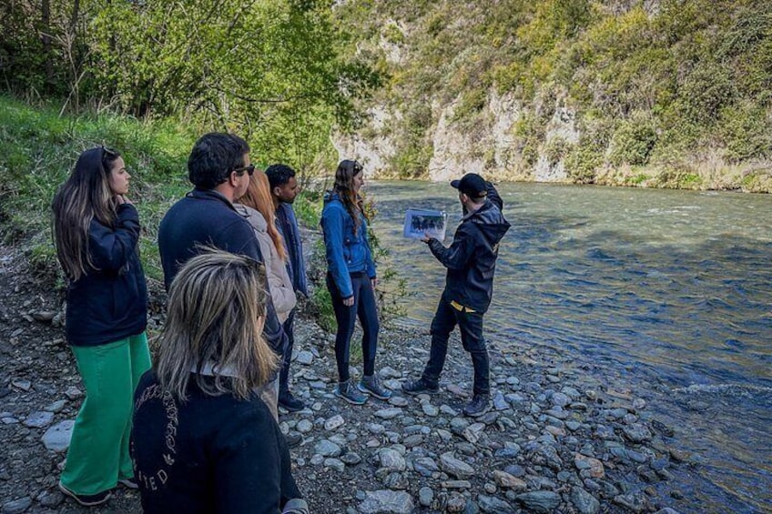 A group of people standing by a river, one person holding a tablet. 4