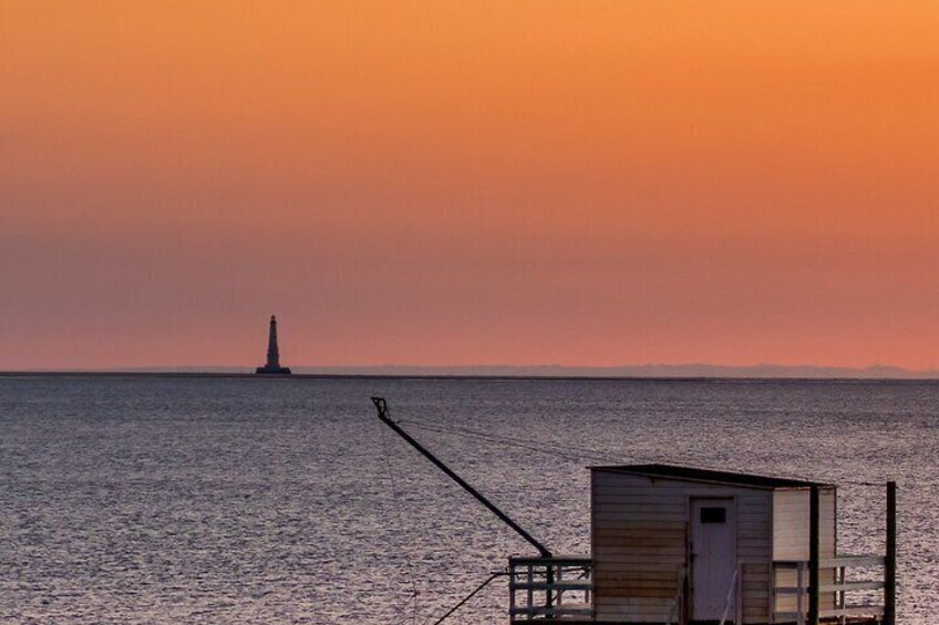 A lighthouse at sunset, a small wooden structure on a pier, and calm water. 1