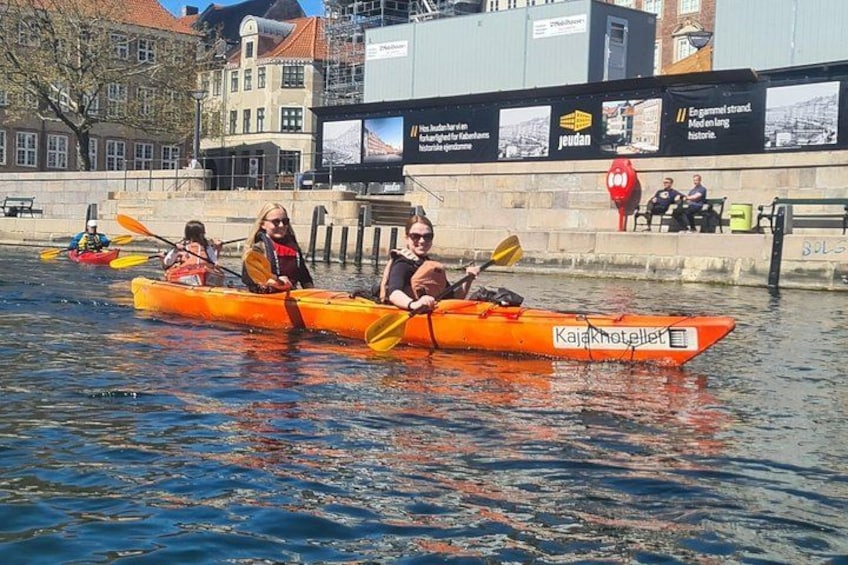 People kayaking on a river with buildings in the background. 3