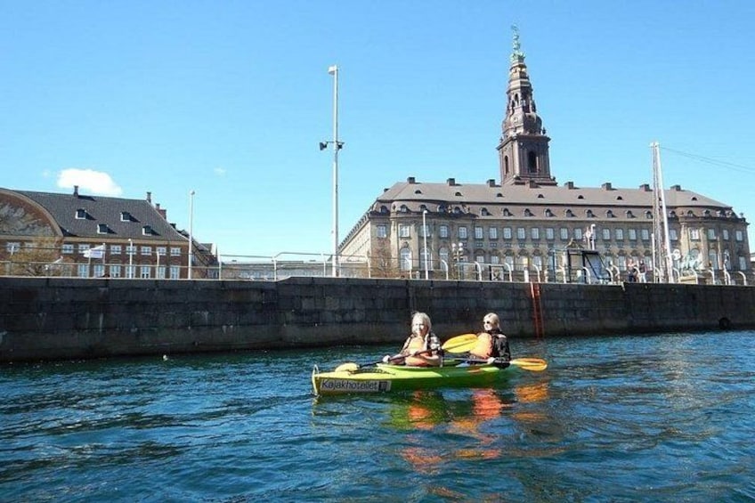 Two people kayaking on a calm body of water with a historic building in the background. 5