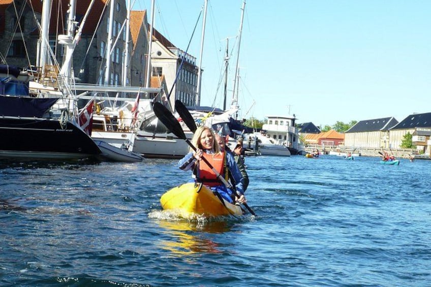 A person kayaking on a yellow kayak in a harbor with boats and buildings in the background. 2