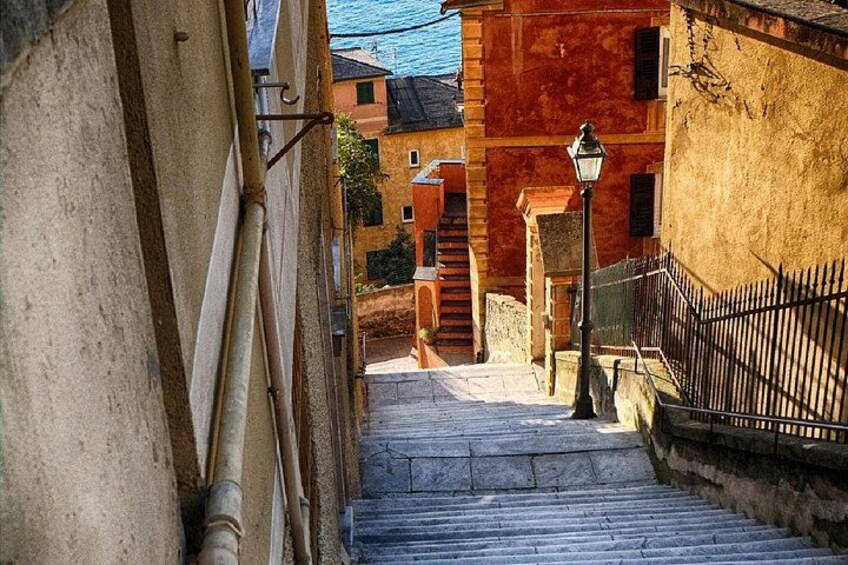 A stone staircase leading down to a street with buildings, a street lamp, and a metal fence. 3