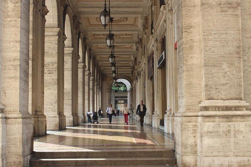 A long corridor with columns, a tiled floor, and hanging lights. 4