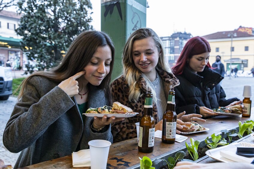 Drei Personen sitzen an einem Tisch mit Essen und Bierflaschen. 1