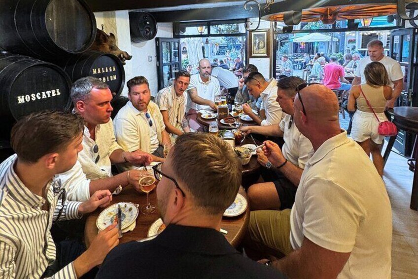 Un gruppo di persone che cenano in un ristorante, con botti di vino sullo sfondo. 5