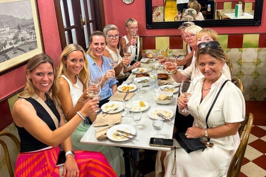Un gruppo di persone sedute attorno a un tavolo in un ristorante, con calici di vino e mentre mangiano. 3