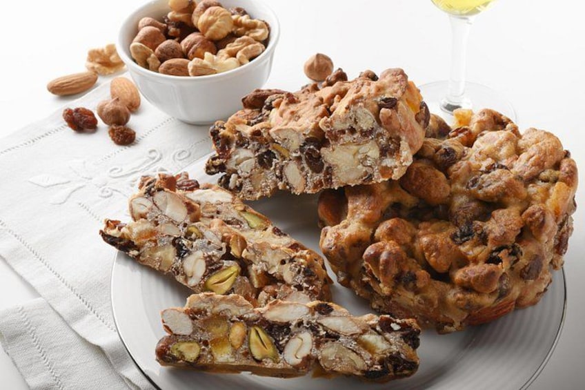 A plate of nut and fruit bars, a bowl of nuts, and a glass of wine. 3