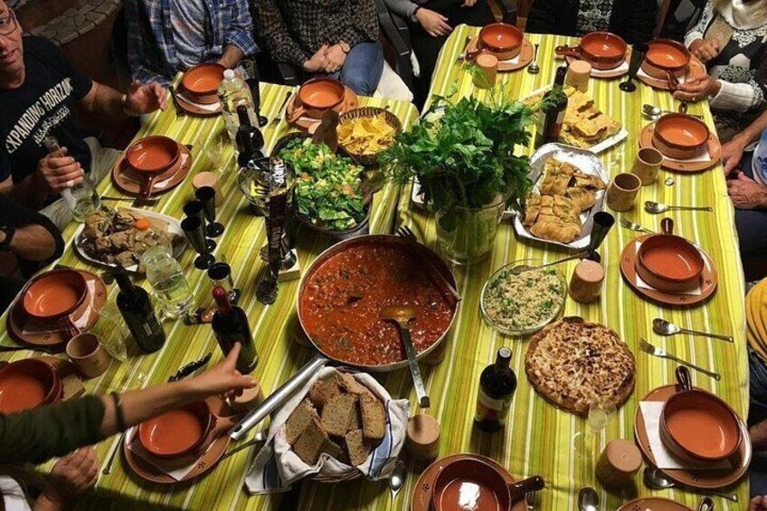 Un groupe de personnes est réuni autour d’une table, devant différents plats, notamment un grand pot de soupe et plusieurs assiettes de nourriture. 4