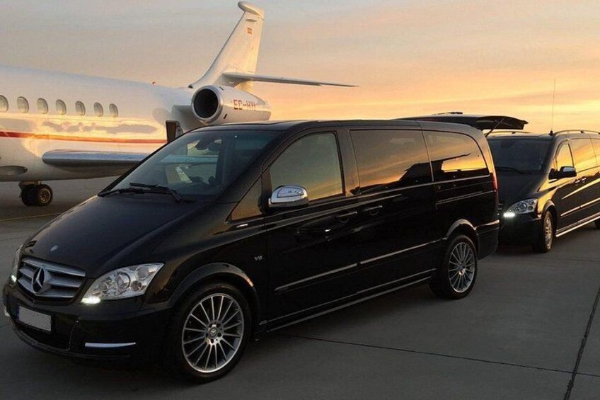 A black Mercedes-Benz van parked on a tarmac with a private jet in the background. 2
