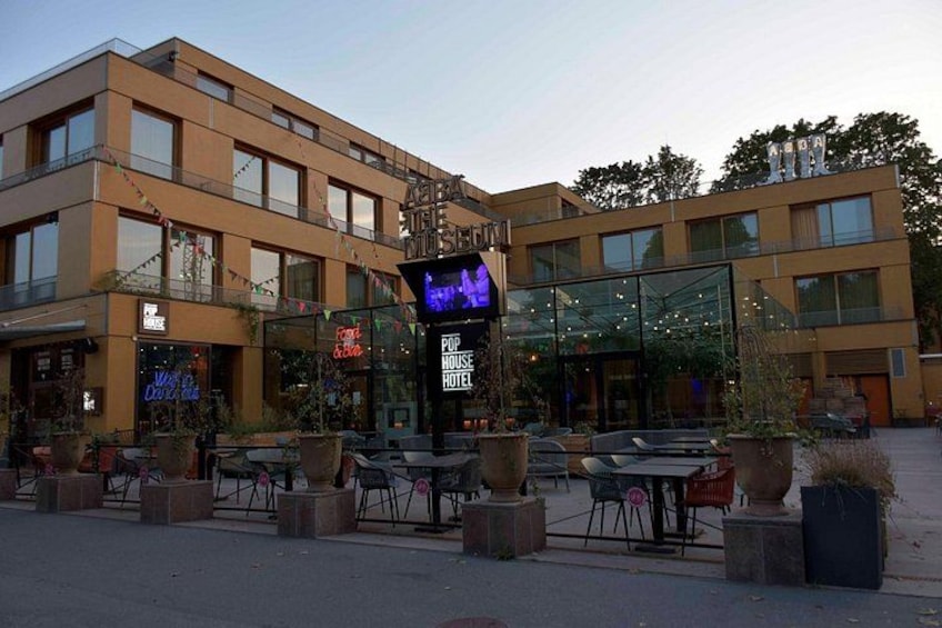 A modern building with a glass facade, outdoor seating area, and a neon sign. 2