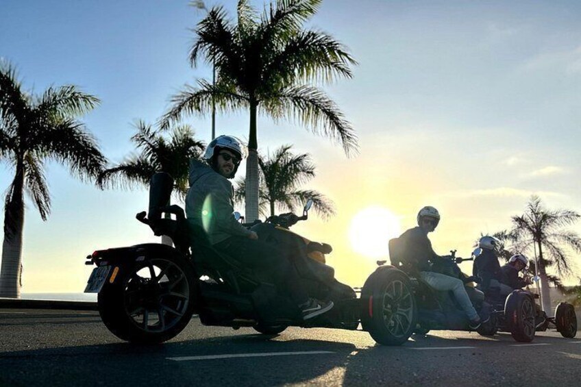 Dos motociclistas en una carretera con palmeras y el sol al fondo. 3