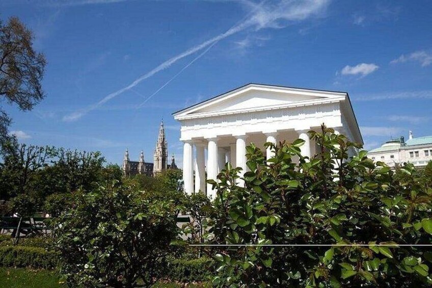 A neoclassical building with columns, surrounded by greenery and a clear blue sky. 4