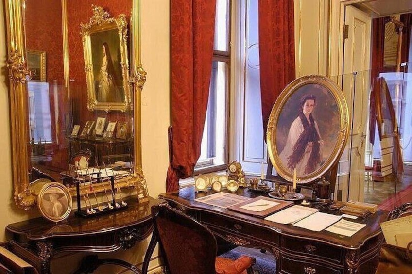 A vintage room with ornate furniture, a piano, and a desk with papers and a mirror. 5