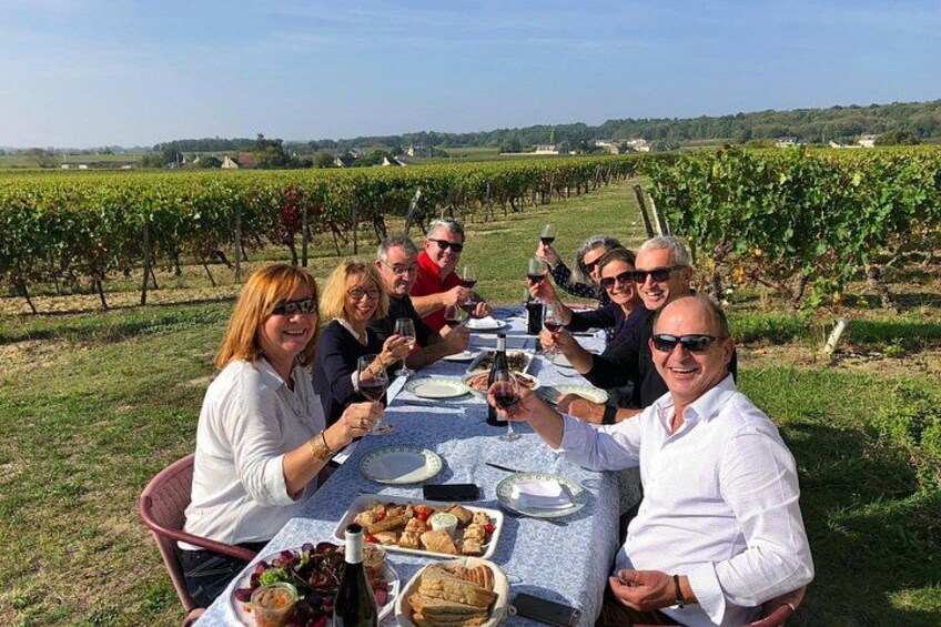 Un grupo de personas cenando al aire libre en un viñedo, con una mesa lista para una comida. 1