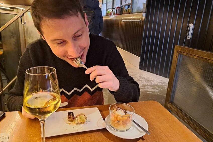 A person sitting at a table with a glass of white wine and a dessert plate. 5