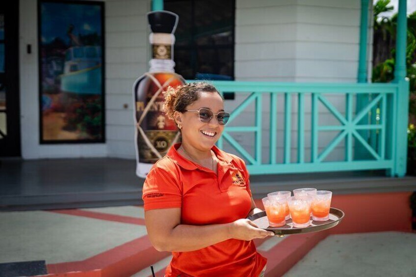 Una persona con uniforme rojo sostiene una bandeja con tres vasos de una bebida rosada. 4