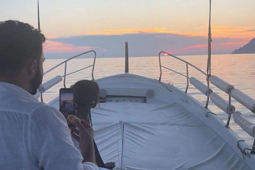 Ein Boot, auf dem eine Person ein Foto macht, mit Geländer und Sonnenuntergang über dem Wasser. 3