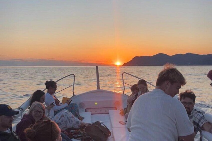 Eine Gruppe von Menschen auf einem Boot bei Sonnenuntergang, die Sonne ist am Horizont zu sehen. 5