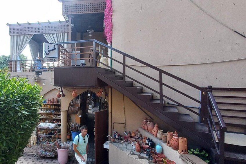 Una escalera conduce a un edificio con un letrero de cafetería, rodeado de plantas en macetas y macetas de barro. 4
