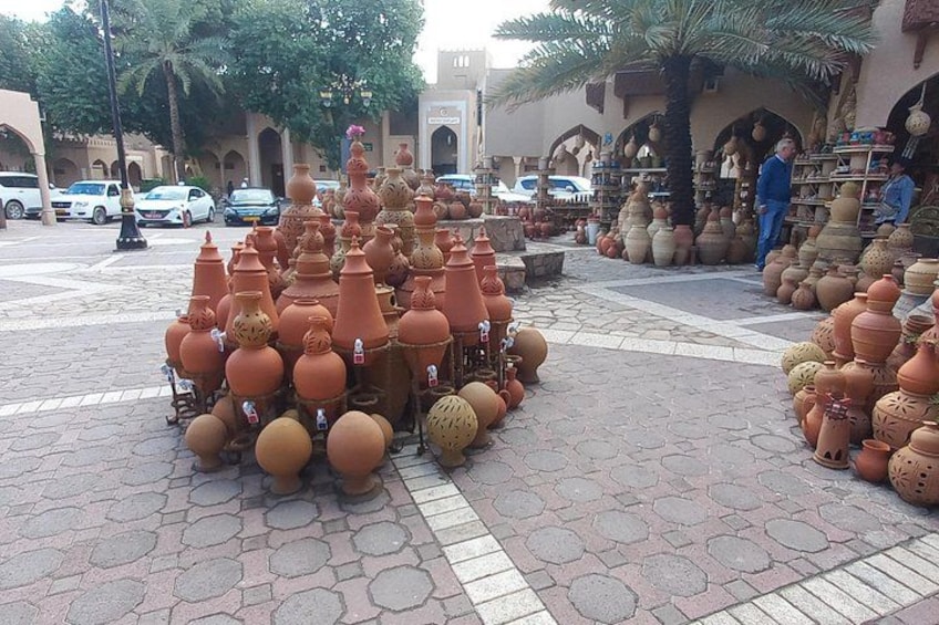 Macetas y jarrones de terracota dispuestos sobre una zona pavimentada, con un edificio y palmeras al fondo. 5