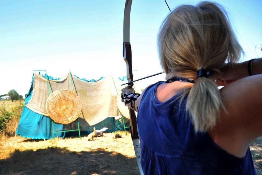 A person with a bow, aiming at a target in an outdoor setting. 5