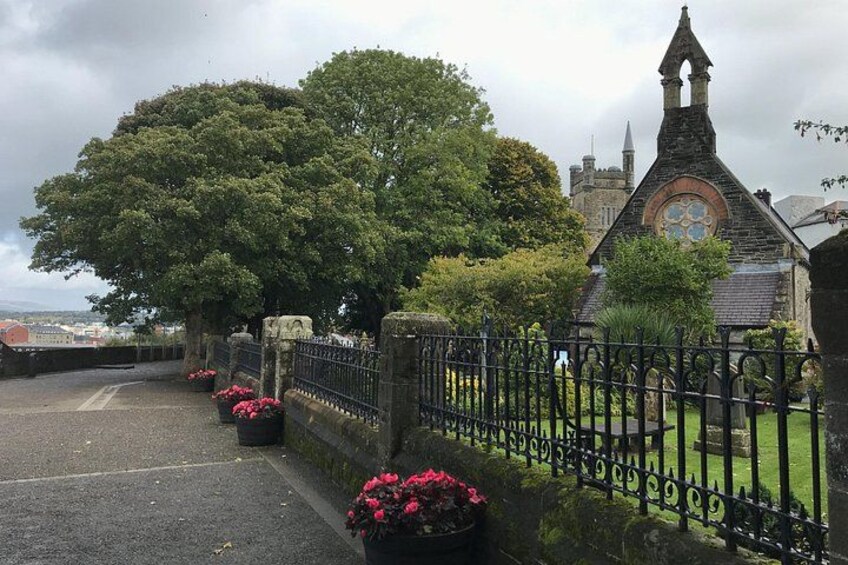 A stone bridge with a metal railing, a large tree, and a church with a pointed steeple. 2