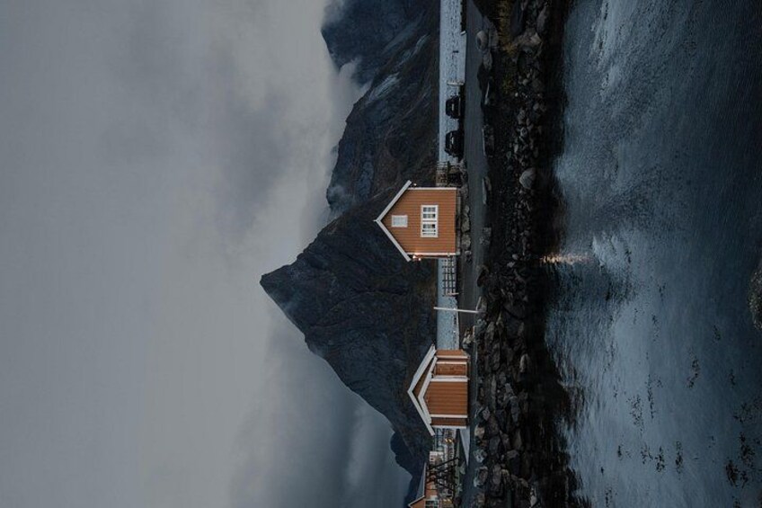 A coastal house with a steep roof, surrounded by rocky terrain and mountains. 2