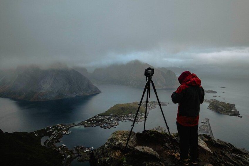 A person with a camera on a tripod overlooking a fjord with mountains in the distance. 1