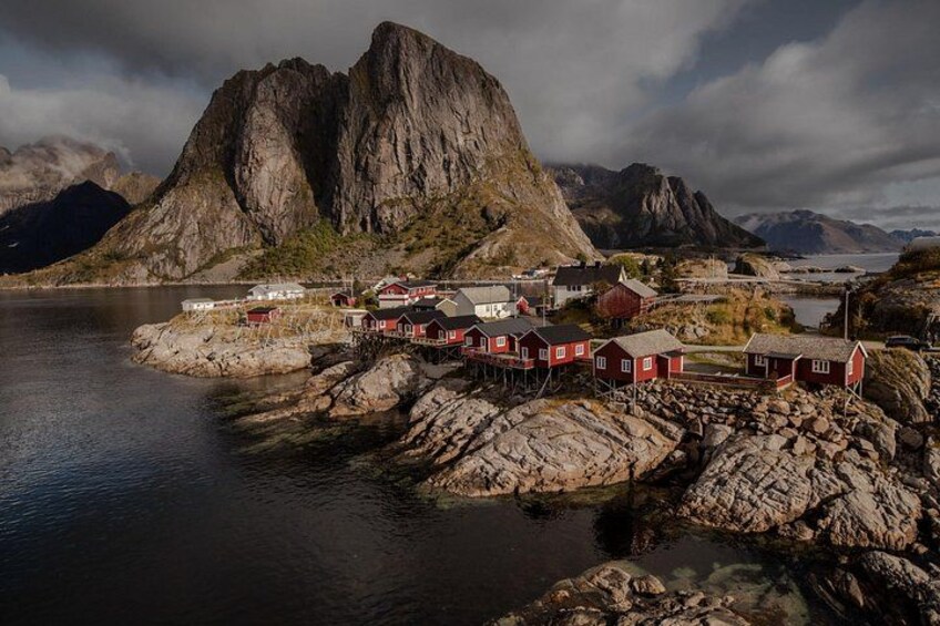 Ein Küstendorf mit roten Häusern, einem Fjord und einem Berg im Hintergrund. 5
