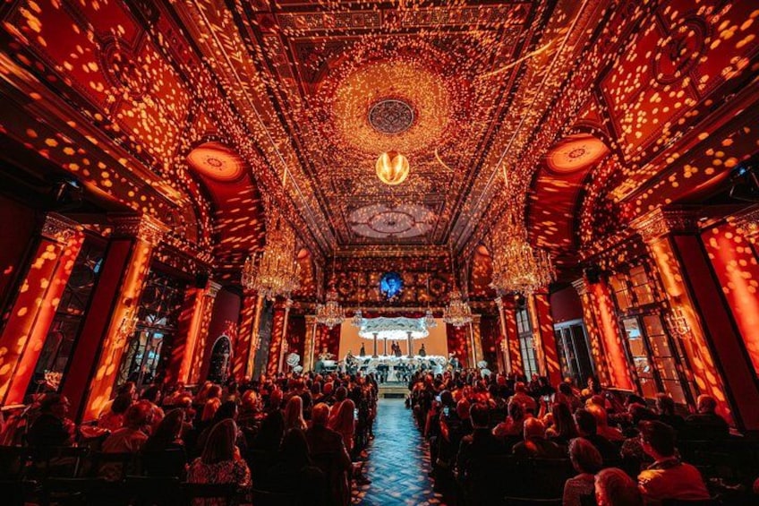 An ornate theater interior with a central stage, rows of seats, and elaborate ceiling decorations. 5