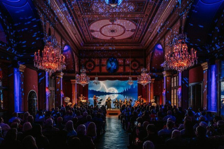 Un teatro con candelabros elaborados, un escenario con artistas y un público sentado en filas. 4