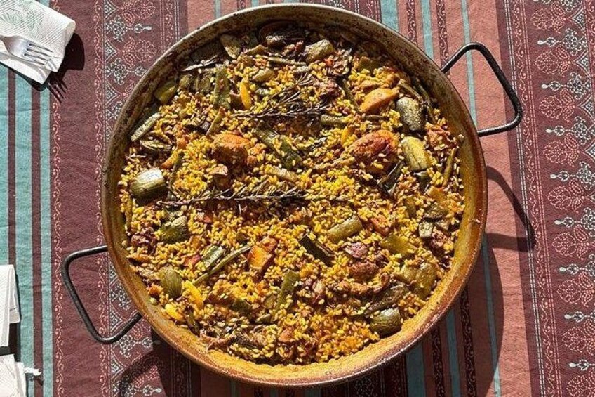 Een grote, ronde, ondiepe pan gevuld met een rijstgerecht met groenten en vlees, geplaatst op een tafelkleed met dessin. 4