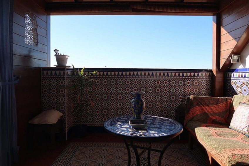 Een terras met een ronde tafel, een plant in pot, een decoratieve vaas en gekleurde kussens. 3