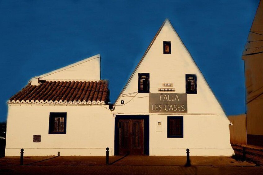 A white building with a sign reading 'FALLA LES CASES' and a tiled roof. 2