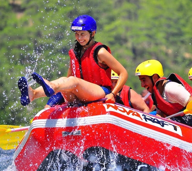 A person in a red life jacket and blue helmet on a red and white watercraft, splashing water. 2