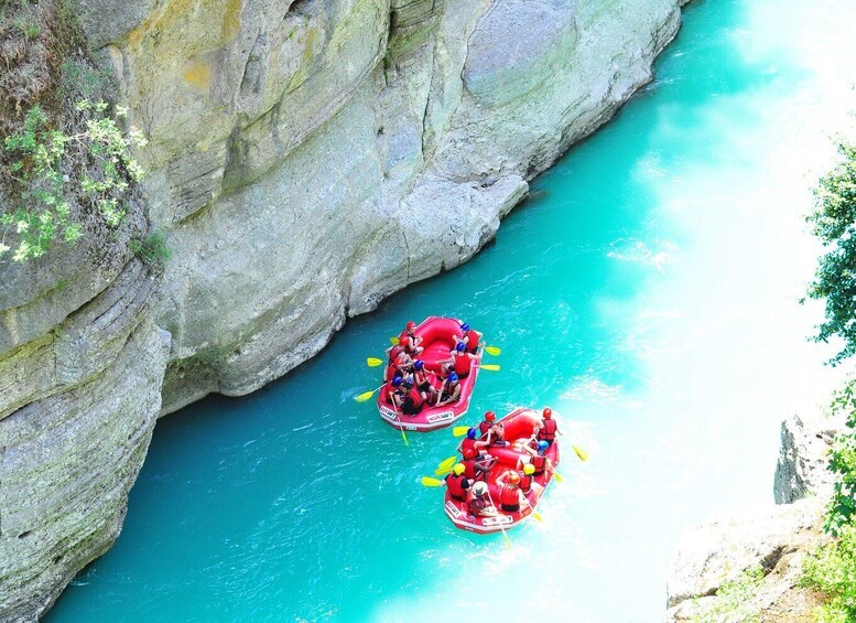 Two red inflatable rafts on a turquoise river surrounded by rocky cliffs. 1