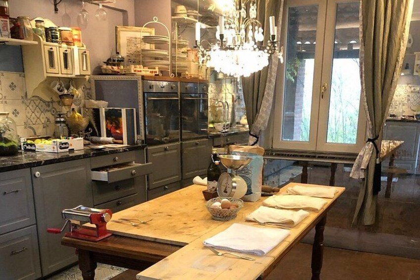 A kitchen with a wooden table, a red pasta maker, and a window with curtains. 4