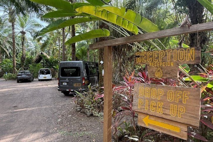 A reception sign, a drop-off pick-up sign, and a van labeled 'Nacaro Costa' parked on a dirt road surrounded by tropical vegetation. 5
