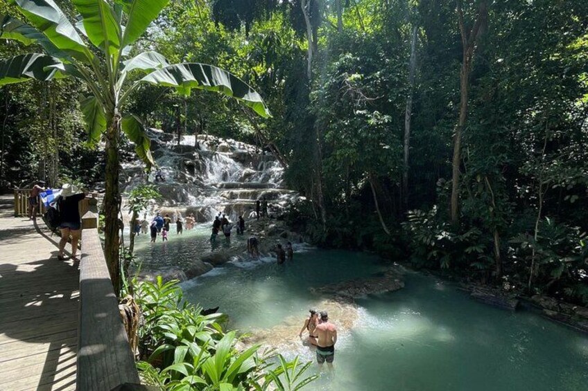 Ein Wasserfall in bewaldeter Landschaft, Personen wandern und schwimmen im Wasser. 5