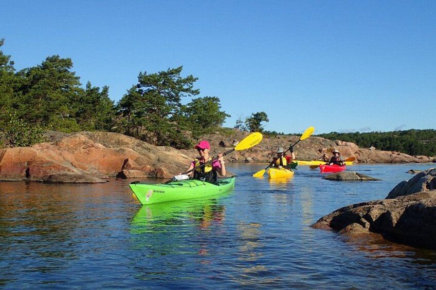People kayaking on a calm river with rocks and trees in the background. 2