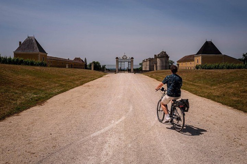 Eine Person fährt Fahrrad auf einem Schotterweg in Richtung eines historischen Gebäudes mit einem Tor. 2