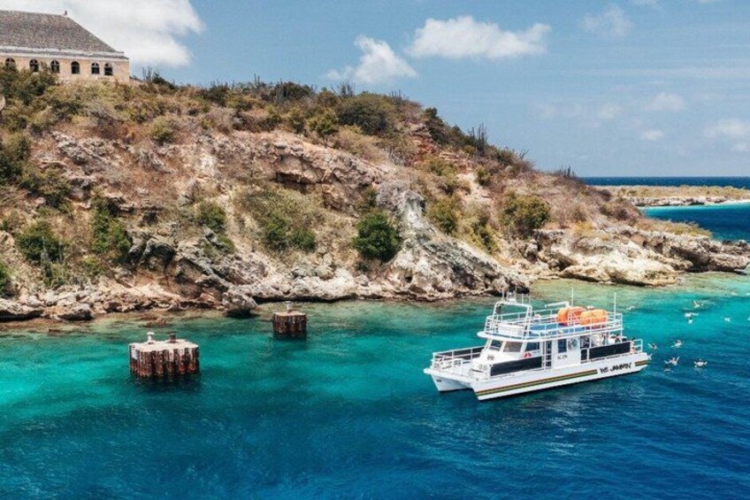 A boat on turquoise waters, a rocky coastline, and a building on a hill. 3
